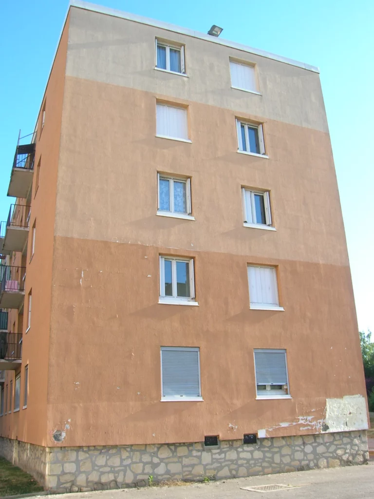 Façade d'immeuble en enduit avec reprises visibles et dégradations en pied de façade, avant diagnostic ETICS