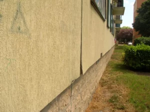 Façade isolée par l'extérieur (ETICS) avec fissure verticale au droit d'un joint de panneaux et désordre en pied de mur